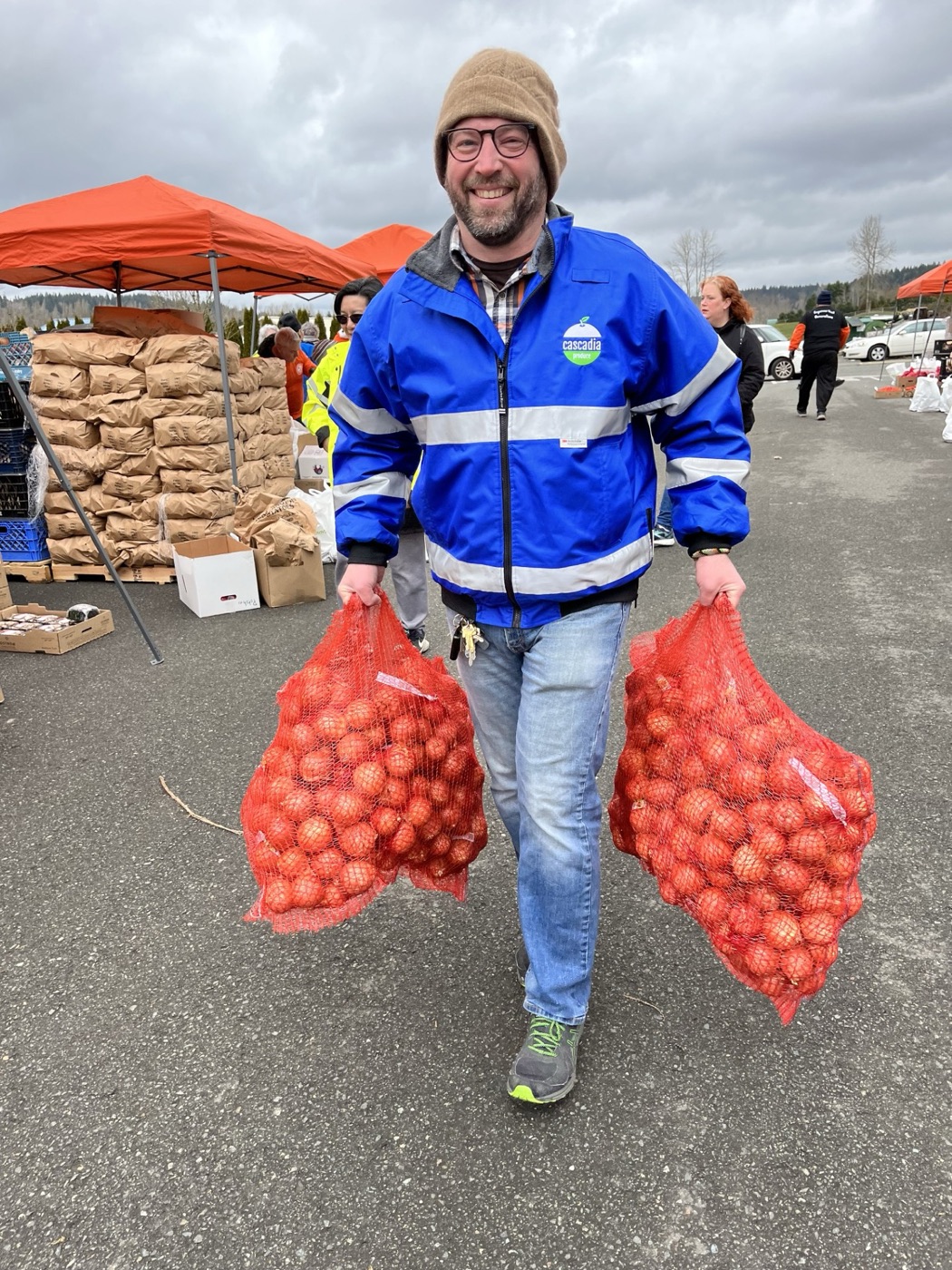 Owner Jeremy Vrablik carrying two big bags of onions at a community food distribution
