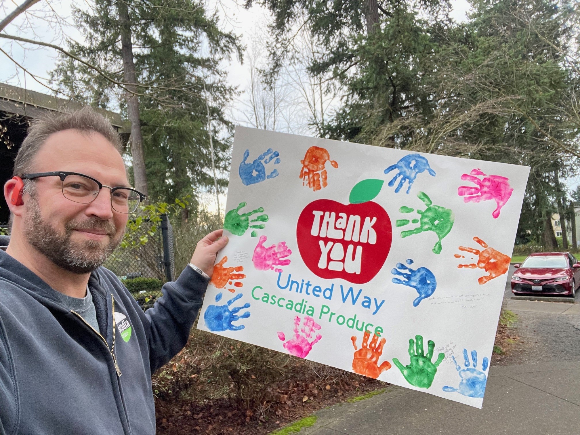 Jeremy Vrablik holding a United Way King County thank-you poster with Cascadia Produce's name and colorful handprints